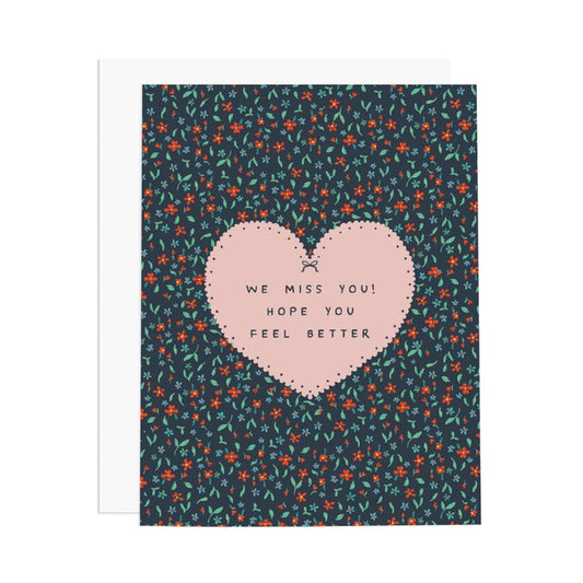 Card with pink heart and text 'We miss you! Hope you feel better' on a floral patterned background
